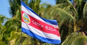 Costa Rica national flag waving against palm trees, symbolizing a peaceful destination for travelers asking is Costa Rica safe