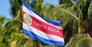 Costa Rica national flag waving against palm trees, symbolizing a peaceful destination for travelers asking is Costa Rica safe